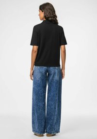 Black short-sleeve polo shirt paired with wide-leg light blue denim jeans, featuring a high waist and frayed hem. Smooth texture, casual design.