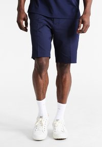 Mörkblå träningsshorts gjorda av lättviktsmaterial, med en skräddarsydd passform. Bärs med vita sneakers och vita strumpor i ankellängd.