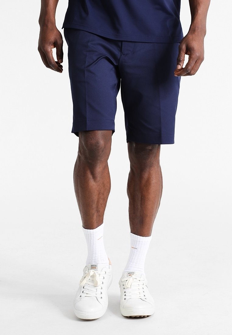 Mörkblå träningsshorts gjorda av lättviktsmaterial, med en skräddarsydd passform. Bärs med vita sneakers och vita strumpor i ankellängd.