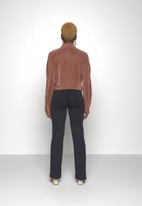 Top metalizado cor-de-rosa de mangas longas com colarinho alto, combinado com calças justas escuras e sapatos de salto de tom claro.