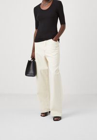 Černý vroubkovaný top s krátkými rukávy doplněný širokými krémovými kalhotami. Doplňky zahrnují malou černou kabelku a černé sandály na podpatku.