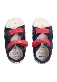 Sandalias azul marino con material de malla, correas de Velcro rojas y suelas perforadas en color beige. Cuenta con una plantilla acolchada y un diseño duradero.