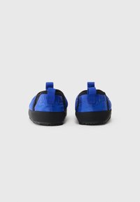Kék anyagú slip-on cipők fekete gumitalppal, kis saroktabokkal és textúrázott felső résszel. Könnyű és rugalmas kialakítás.