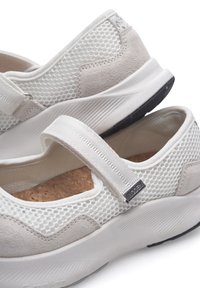 Zapatillas blancas con parte superior de malla y acentos de ante, que cuentan con una correa de Velcro y una plantilla de corcho texturizado. Suela de goma con una ligera elevación.