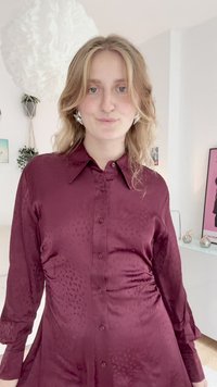 Camisa bordeaux, de cetim, com botões, de mangas longas e padrão texturizado subtil. Apresenta um colarinho e uma bainha ligeiramente rodada.