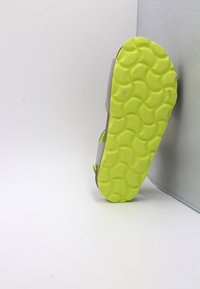 Chaussure de sport avec une semelle extérieure flexible et texturée en vert lime vif, une tige grise, et des détails d'accent dans des couleurs néon assorties.