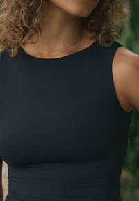 Marineblaues ärmelloses Kleid mit glattem Material, eng anliegendem Design und rundem Ausschnitt. Dünne goldene Halskette um den Hals getragen.