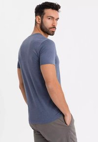 T-shirt da uomo a maniche corte in cotone blu scuro, con vestibilità classica e colletto rotondo, mostrato di spalle con le mani nelle tasche.