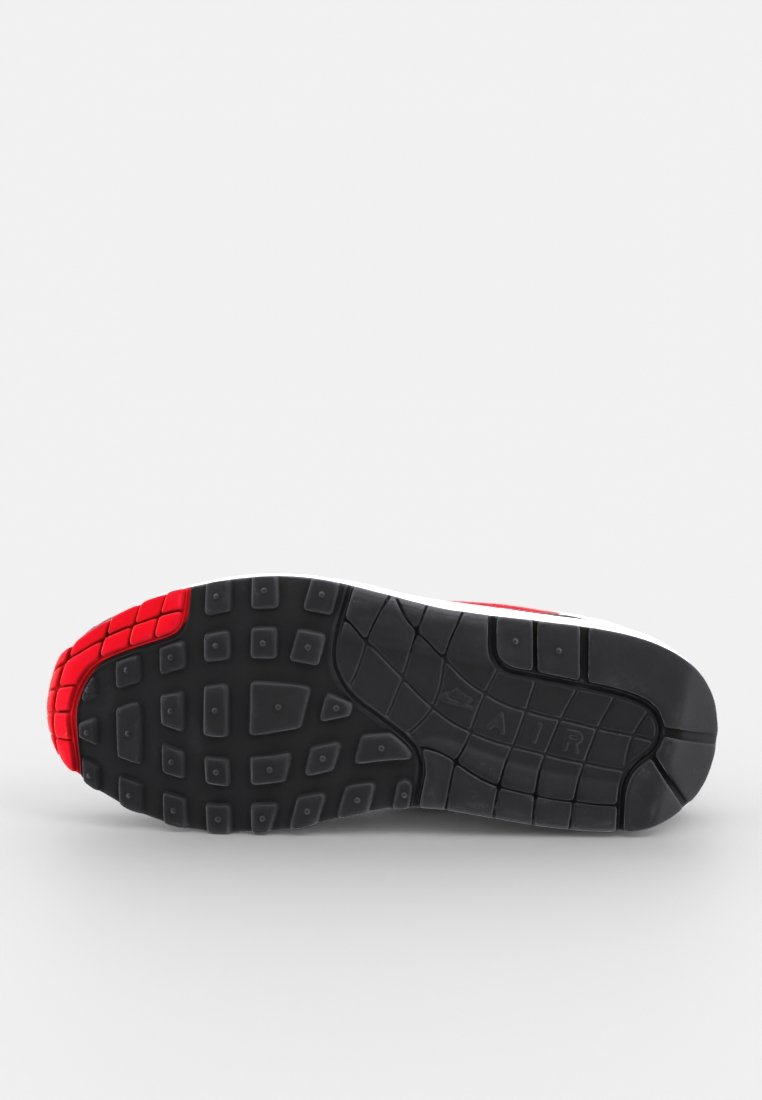 Semelle de sneaker avec une base en caoutchouc noir, sections rouges, motif de bande de roulement texturé et rainures prononcées pour une traction et une flexibilité accrues.