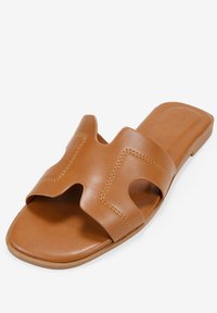 Sandalo scivoloso in pelle color cuoio con una larga fascia e un design a taglio, texture liscia, suola piatta e dettagli di cucitura in contrasto.