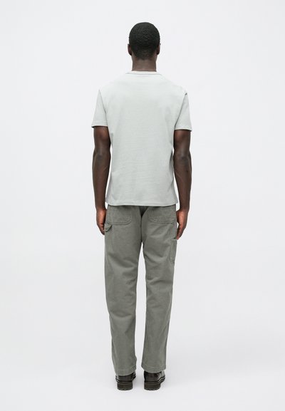 Svetlosivé tričko s okrúhlym výstrihom, skombinované s olivovo zelenými cargo nohavicami s bočnými vreckami. Model stojí chrbtom k divákovi.