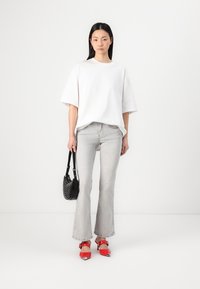 T-shirt blanc surdimensionné, jeans gris clair évasés, sandales à talons rouges avec des accents argentés, et un sac à main circulaire noir.