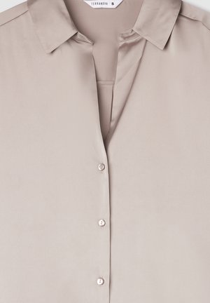 Camicia button-up di un beige chiaro realizzata in tessuto liscio, con colletto classico e bottoni simili a perle lungo la parte anteriore.
