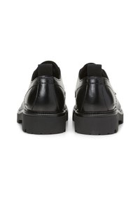 Zapatos de cuero negro con un acabado suave, punta redondeada, paneles laterales elásticos y suelas de goma resistentes. Presentan un diseño elegante y minimalista.