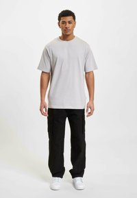 Lys grå bomulds T-shirt med korte ærmer, parret med sorte cargo bukser med lommer og hvide sneakers. Enkel design og afslappet pasform.