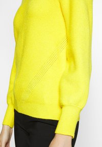 Gelber strukturierter Strickpullover mit einem diagonalen Muster und gerippten Bündchen, der über ein cropped Design und eine taillierte Silhouette verfügt.