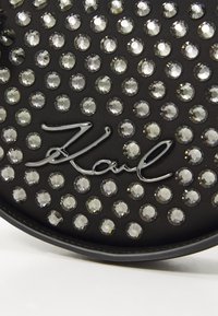 Black textured material featuring circular rhinestones arranged in a grid pattern, with a glossy silver "Karl" signature.