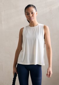 Lichte, mouwloze sporttop in gebroken wit, met een ontspannen pasvorm en een gladde textuur, gecombineerd met donkerblauwe legging met strepen.