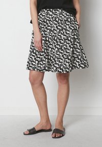 Jupe à motifs noir et blanc avec une taille élastique et des poches latérales. Des sandales noires plates complètent la tenue.