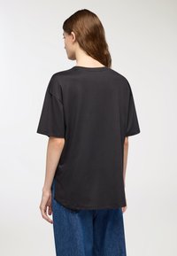 T-shirt nero oversize con maniche corte, collo rotondo e texture liscia. Presenta un fit rilassato e scende leggermente più lungo sul retro.