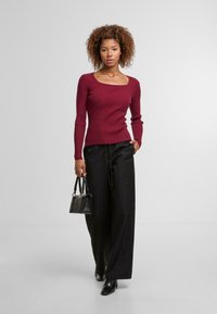 Burgundský žebrovaný top s dlouhým rukávem a čtvercovým výstřihem, kombinovaný s širokými černými kalhotami a malou černou kabelkou. Hladká textura, přiléhavý střih.