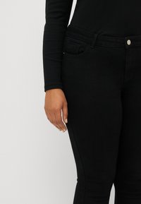 Jean en denim noir à coupe slim, avec une poche frontale, des coutures discrètes et une fermeture à bouton en métal argenté à la taille.
