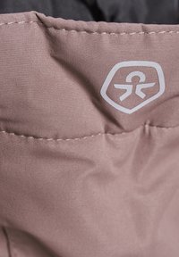 Mjuk rosa tyg med en texturerad yta, prytt med en vit logotyp. Sömmen är ordentligt sydd, vilket framhäver en slät och hållbar design.