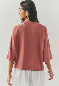 Top tricoté rose, texturé, avec un col rond et des manches trois-quarts, affichant un design court et de légers détails raglan.