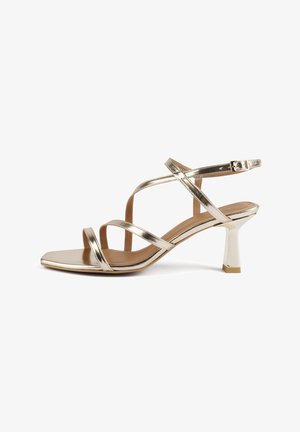 Gold metallic heeled sandal with multiple crisscross straps. Square toe design, shiny finish, and a flared block heel. Smooth interior.