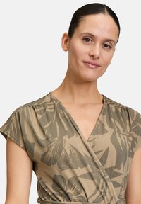Robe portefeuille en tissu vert olive avec un motif floral, manches courtes et décolleté en V. Texture douce avec une coupe confortable.