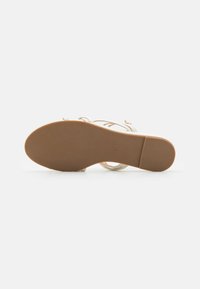 Beige hælhæl sandal med krydsede stropper, glat læderoverflade, lukket tå, flad gummisål og en lille hæl med størrelse markeret.