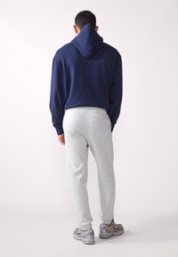 Marineblauer Kapuzenpullover mit großer Kapuze, kombiniert mit hellgrauen Jogginghosen. Die Hosen haben eine taillierte Passform und eine weiche Textur. Silberne Sportschuhe.