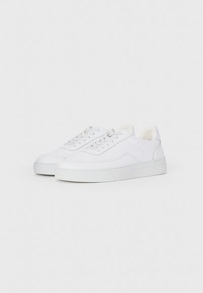 Un paio di sneakers bianche sportive con lacci, upper in pelle liscia e suole in gomma piatta su uno sfondo bianco uniforme.