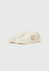 Cream-colored sneakers with textured panels, including tan accents, featuring a star logo, lace-up design, and a solid rubber sole.