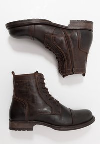 Botines de cuero marrón con un acabado suave, que presentan un diseño con cordones, cremallera lateral y detalles de costura en la parte superior y la suela.
