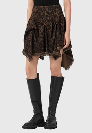 Spódnica w cętki lamparta w ciemnobrązowym kolorze z frędzlami na dole, zestawiona z wysokimi czarnymi skórzanymi botkami na masywnej podeszwie.