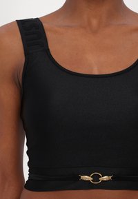 Top corto nero con spalline larghe decorato con il testo "JUST". Tessuto liscio con dettaglio ad anello dorato in vita, accentuato da elementi decorativi a forma di serpente.