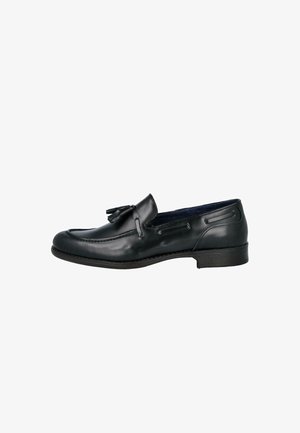 Mocasín de hombre de cuero negro con borlas, punta redonda y tacón bajo, visto de lado sobre un fondo blanco.