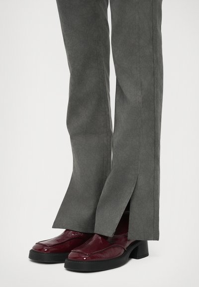 Σκούρο κόκκινο λουστρίνι μποτάκια με τακούνι συνδυασμένα με γκρι παντελόνι που έχει μπροστινές σχισμές στο στρίφωμα.