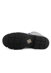 Semelle de botte en caoutchouc noir avec motif de texture antidérapant, crampons rectangulaires et logo de marque sur la section du talon.