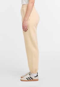 Beige Sweatpants mit einem elastischen Bund und Bündchen an den Knöcheln. Hergestellt aus einem weichen Stoff, der eine glatte Textur und eine entspannte Passform zeigt.