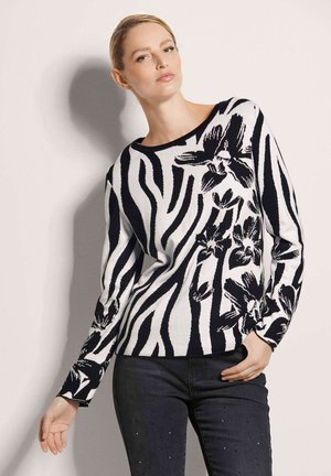 Schwarz-weiß gestreifter Pullover mit floralen Akzenten, runder Ausschnitt und langen Ärmeln, kombiniert mit dunklen Jeans mit Nieten-Details.