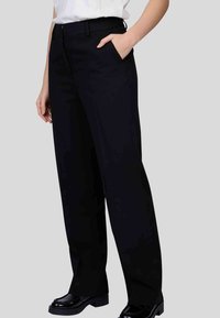 Pantalons noirs taille haute avec une coupe droite, des poches latérales et une finition lisse, associés à des chaussures noires brillantes.