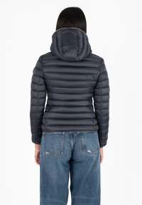 Zwarte pufferjack met een capuchon, voorzien van een gequilt design en geribbelde zoom. Gekoesterd met lichtblauwe hoge taille jeans.