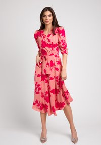 Różowa sukienka owijana z odważnymi czerwonymi wzorami kwiatowymi, z rękawami o długości trzech czwartych i paskiem w talii; miękki materiał z lekko falującą, midi długością spódnicą.
