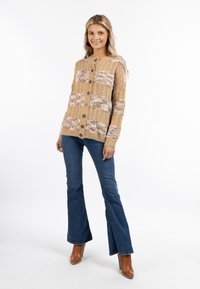 Stickad cardigan i beige med färgglada blomstermönster, med en rund halsringning, knäppning och ribbade ärmar. Matchas med utsvängda jeans.