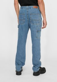 Light blue denim cargo pants with multiple pockets, straight-leg fit, and leather patch at the waistband. Worn with black footwear.