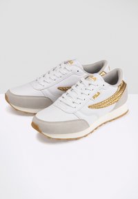 Baskets blanches avec accents dorés, dessus en tissu texturé, superpositions en daim gris, et design à lacets. Semelle en caoutchouc avec adhérence texturée.