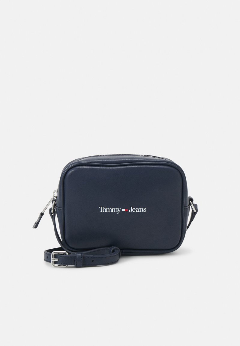 Bolso bandolera de cuero azul marino con cierre de cremallera, correa ajustable y logo blanco "Tommy Jeans" en el frente. Forma rectangular, textura suave.
