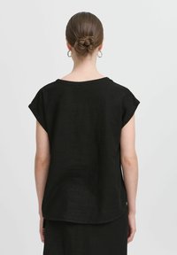 Top in lino nero con maniche corte, vestibilità comoda, scollatura rotonda e orlo curvo. Indossato con una gonna nera abbinata.